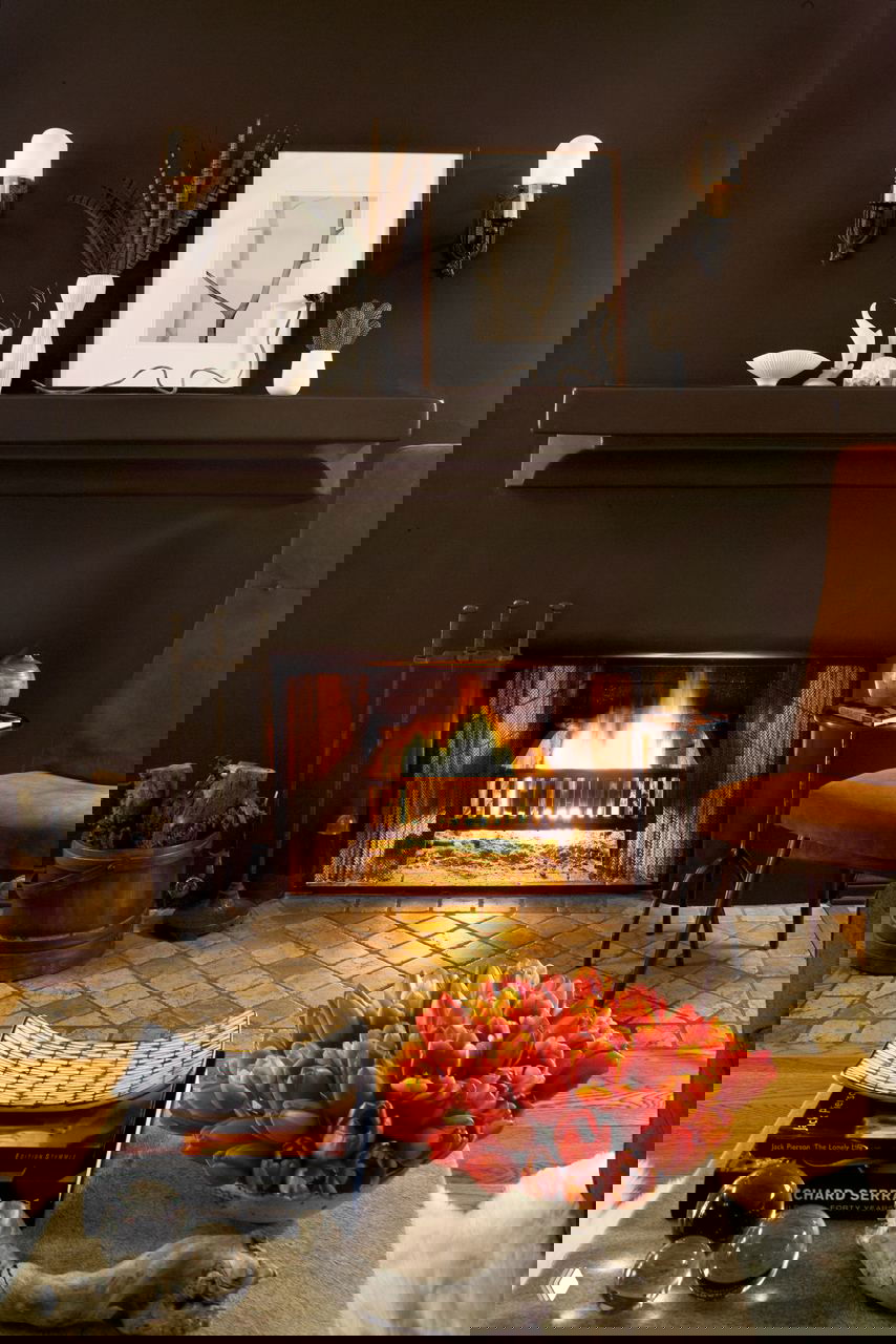 Тёплый интерьер с камином, тёмно-коричневыми поверхностями, уютным креслом и букетом тюльпанов на столике — сочетание для комфортной атмосферы.