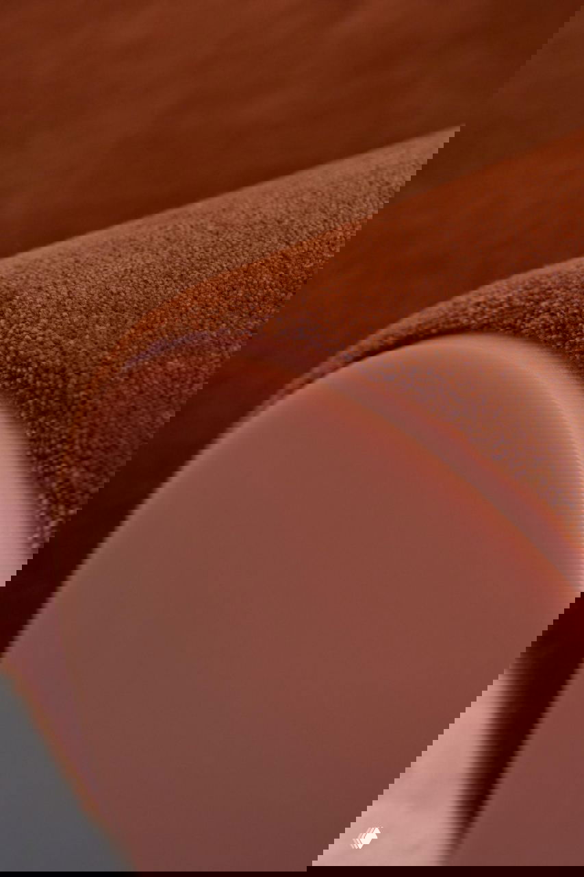 Крупный план изогнутого подлокотника: фактура бордовой шерсти, плавная форма и глянцевая вставка из смолы на торце в одном кадре.