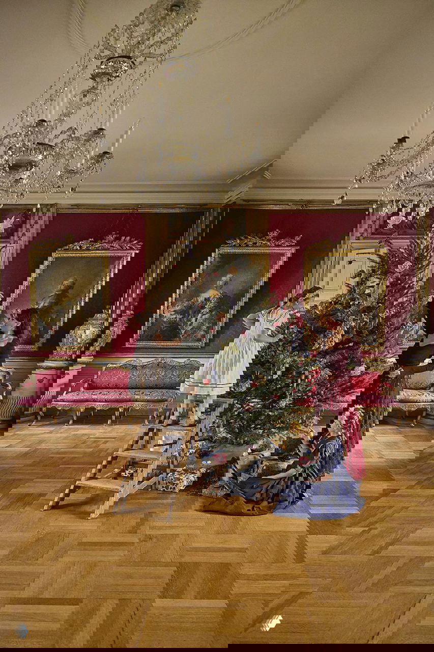 Бальный зал поместья: дети и хозяйка Клара Розенкранц украшают рождественскую ёлку среди антиквариата, кресел и больших картин в золочёных рамах на Рождество в поместье на Фюне.