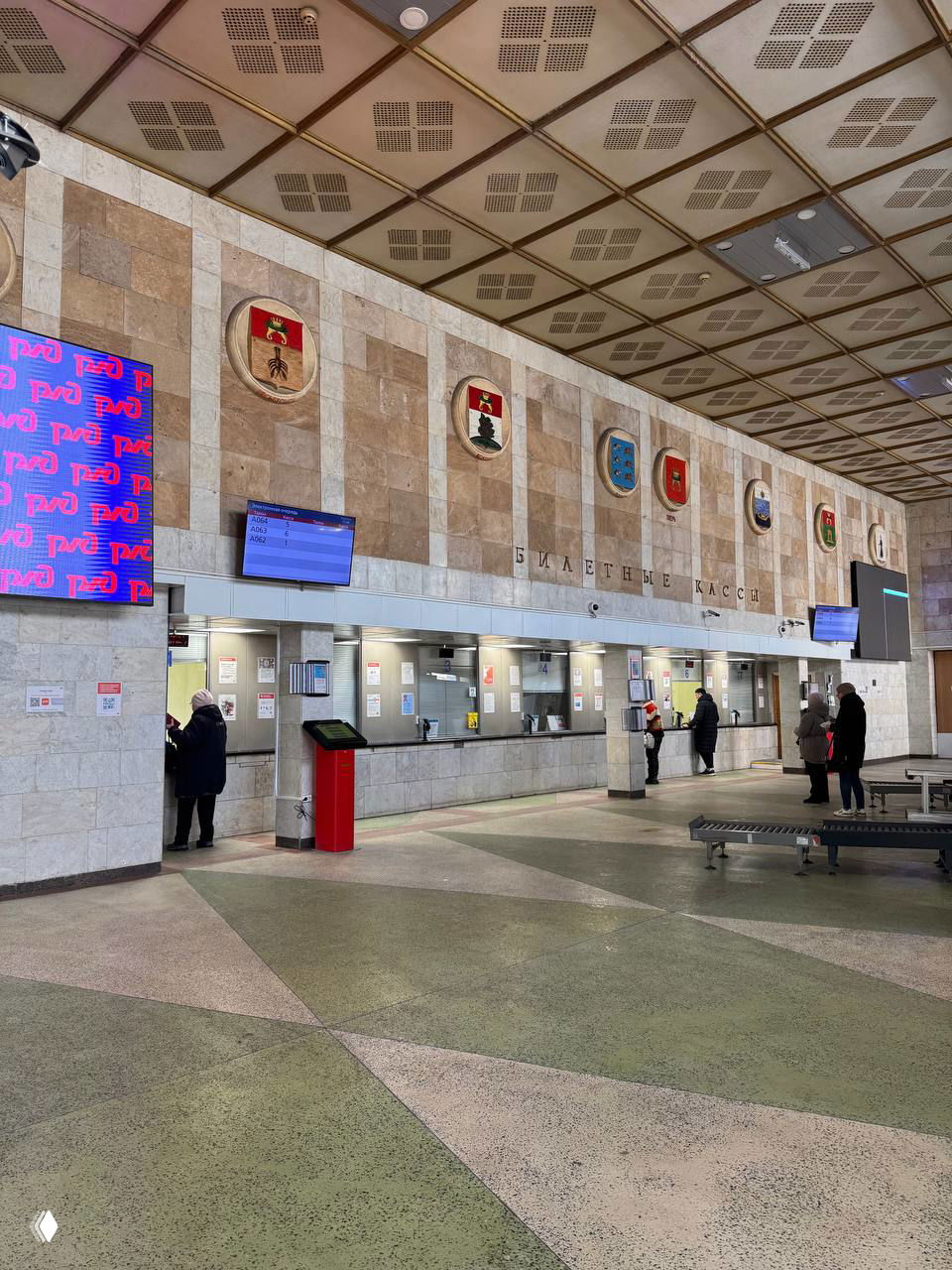 Кассовый зал Тверского вокзала с мраморными стенами, электронными табло и просторным полом с геометрическим узором, часть интерьера в советском стиле.