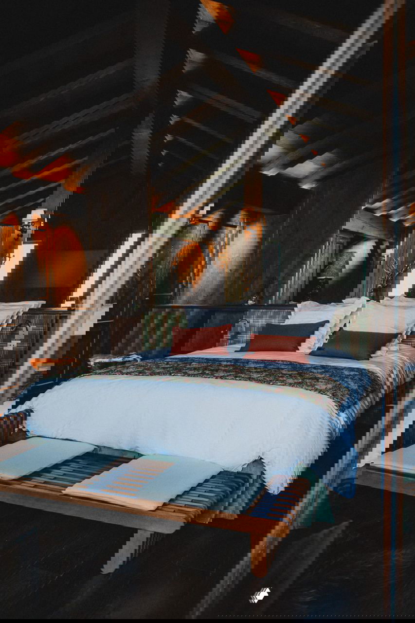 Спальня в шале с большим кроватным местом, тёплым деревянным интерьером, открытыми балками и текстилем в клетку, создающими уютную альпийскую атмосферу.