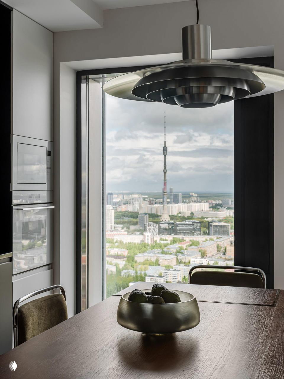 Подвесной светильник в фокусе на фоне большого окна с видом на город; композиция подчёркивает форму и индустриальную эстетику объекта.