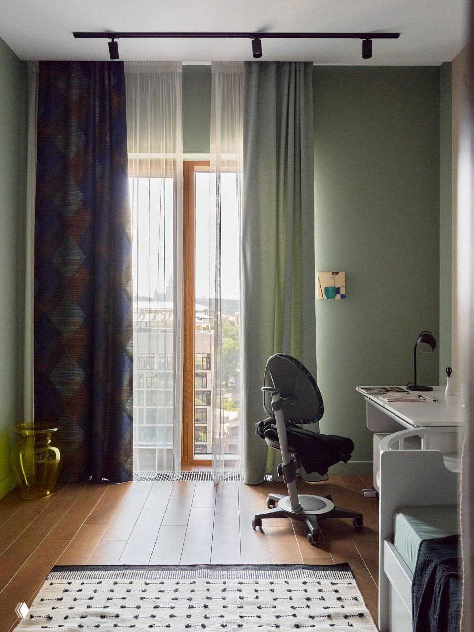 Уютная спальня с фиолетовым изголовьем и декоративным зелёным прикроватным комодом в стиле ретро на фоне широкого окна с видом на город.