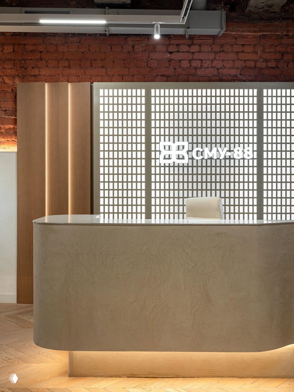 Стойка ресепшн с мягкой округлой формой и подсветкой, на фоне светящейся декоративной панели и кирпичной стены — чистая лаконичная рецепция офиса.