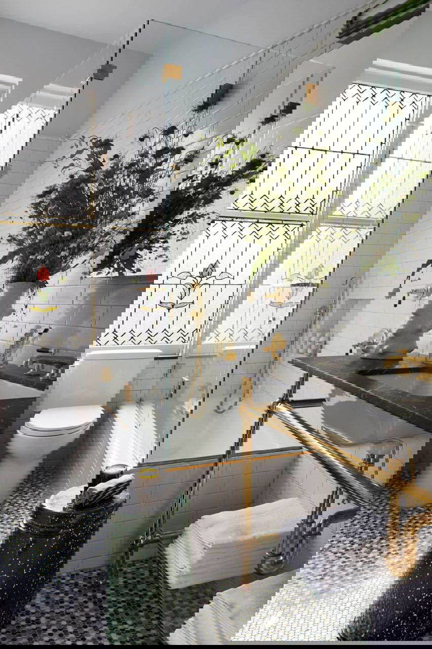 Ванная комната с мозаичным полом, стеклянной перегородкой и золотистой сантехникой; сочетание винтажных и современных элементов.