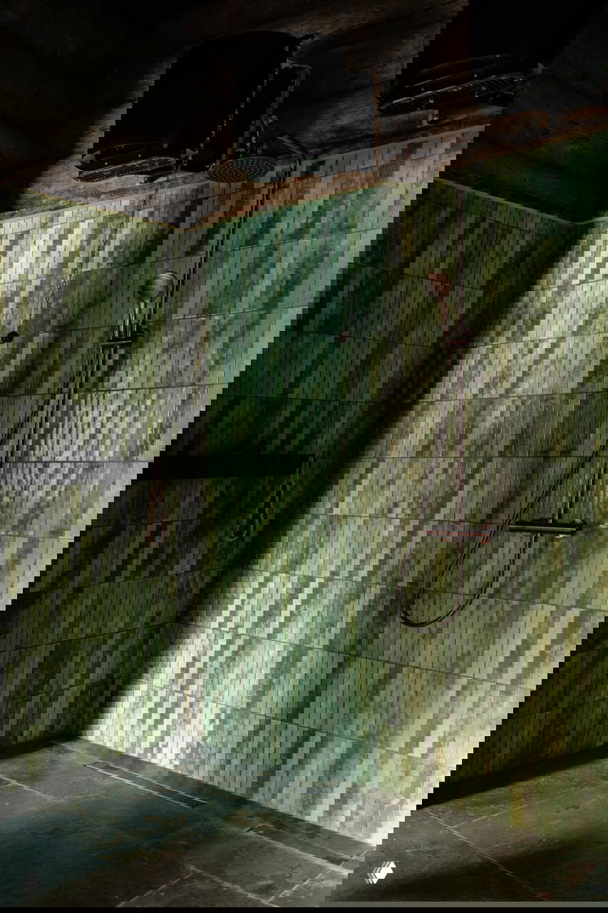 Парная/душевая зона с зелёной плиткой в тон натуральным материалам, бронзовой сантехникой и тёмным полом в интерьере банного дома.