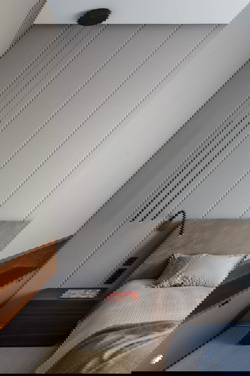 Спальня с вертикальной мягкой панельной отделкой в серых тонах, низкой кроватью с текстильной обивкой и лаконичным прикроватным столиком, спокойная палитра.