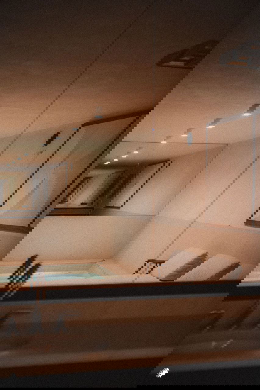 Подвальное пространство с небольшим бассейном и лежаками, спокойная светлая зона для отдыха внутри шале, минималистичный дизайн бассейна.