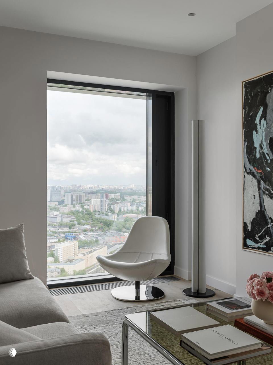 Уютный уголок у панорамного окна: белое кресло, низкий столик и вид на городской ландшафт Москвы — лёгкая, спокойная композиция.