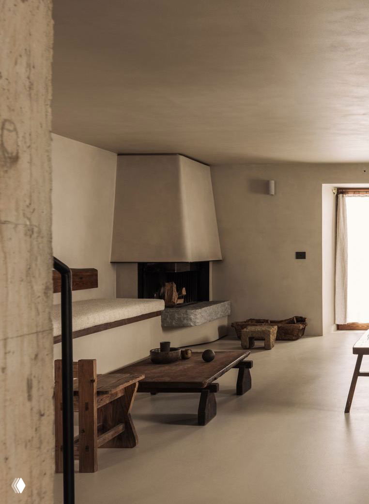 Гостиная с низким деревянным столом, встроенными лавками из вощеного бетона и камином — сочетание ваби-саби и альпийского уюта в доме Maison Osaïn.