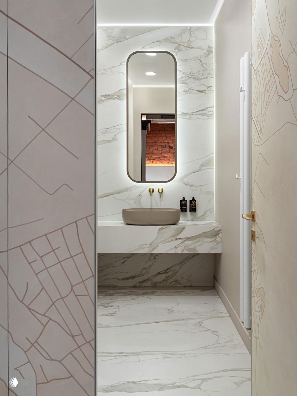 Санузел в офисе с белым мраморным покрытием, овальным зеркалом с подсветкой и минималистичной раковиной — аккуратная отделка мелких помещений.