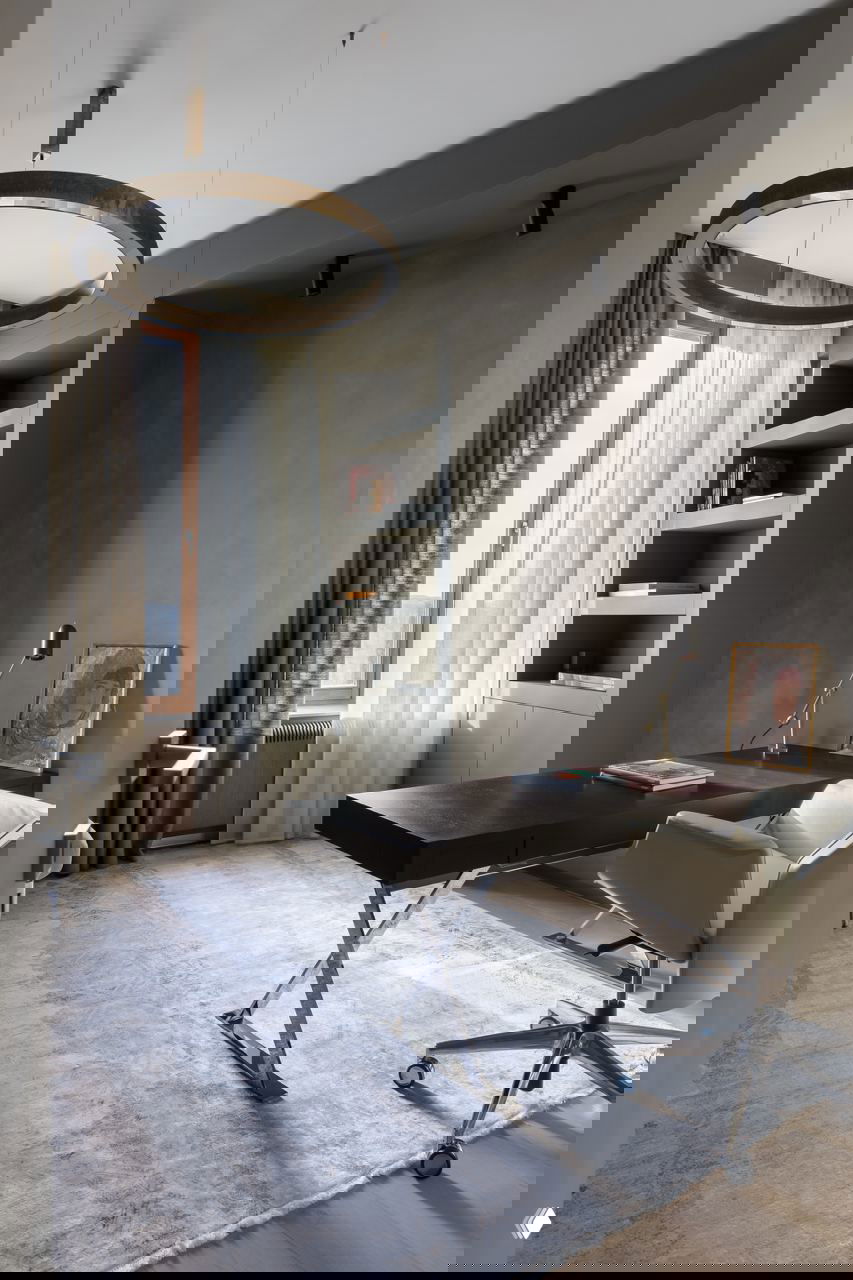 Кабинет с большим деревянным рабочим столом, открытыми полками и креслом на колёсах у окна — минималистичное пространство для работы с естественным светом.