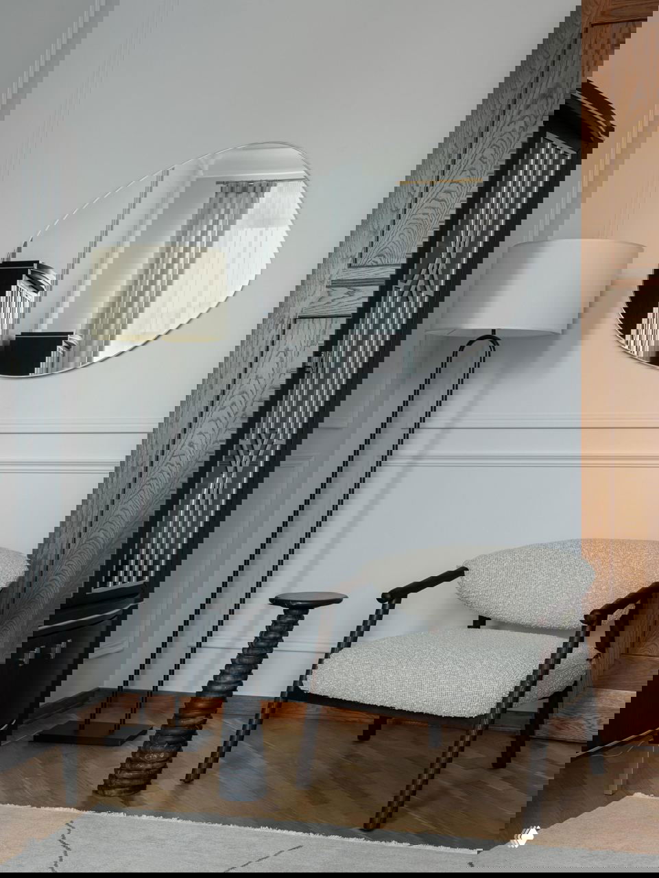 Уютный угол с креслом, напольной лампой и асимметричным зеркалом на стене — детали, формирующие интимную атмосферу пространства.