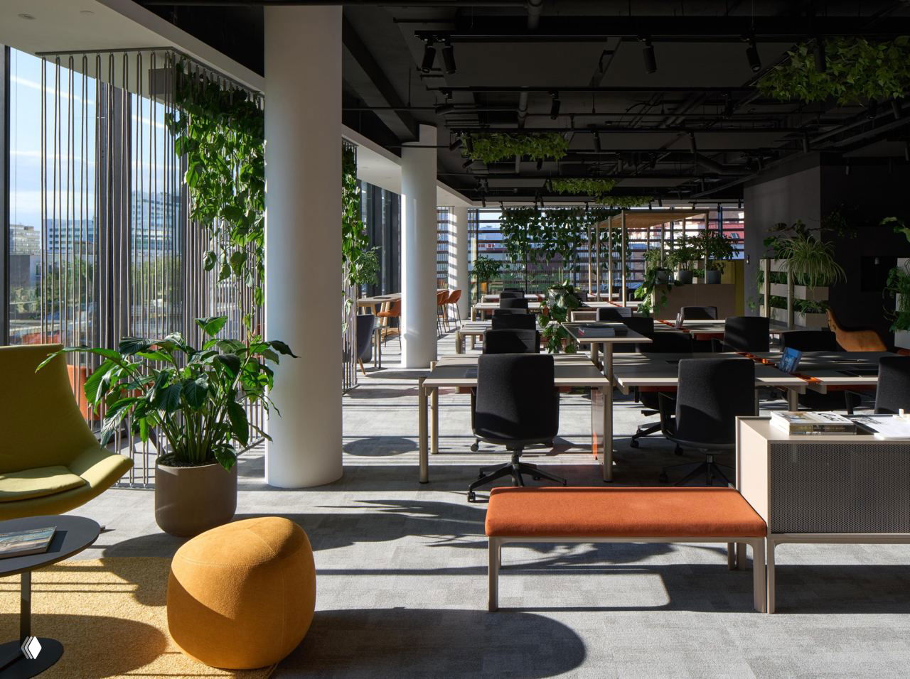 Открытое рабочее пространство с панорамными окнами, рабочие столы, высокие колонны и яркие жёлто‑оранжевые пуфы