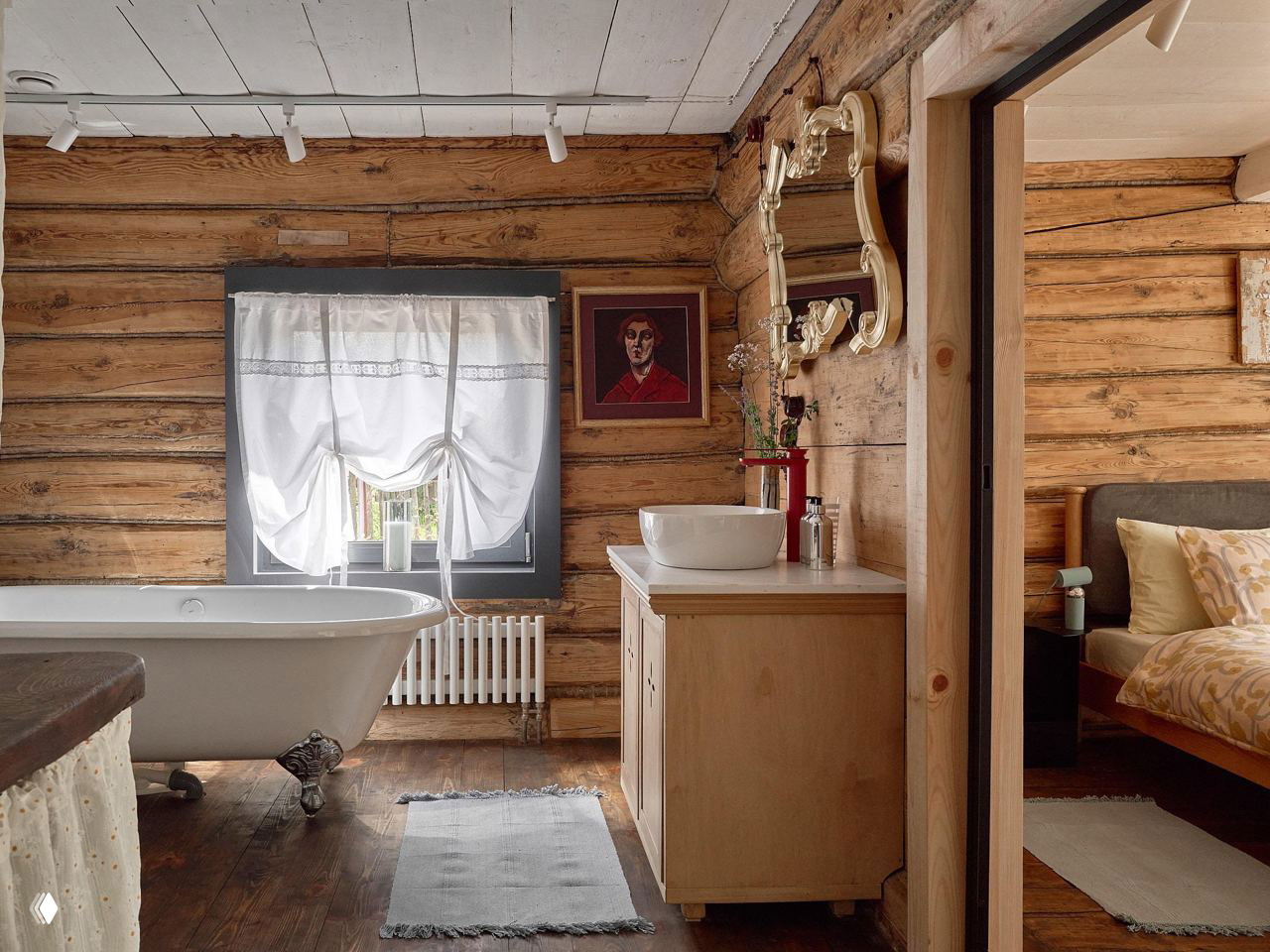 Ванная комната в деревянном доме: большая чугунная ванна, раковина на деревянной тумбе и окно с видом на сад создают провинциальный шарм.