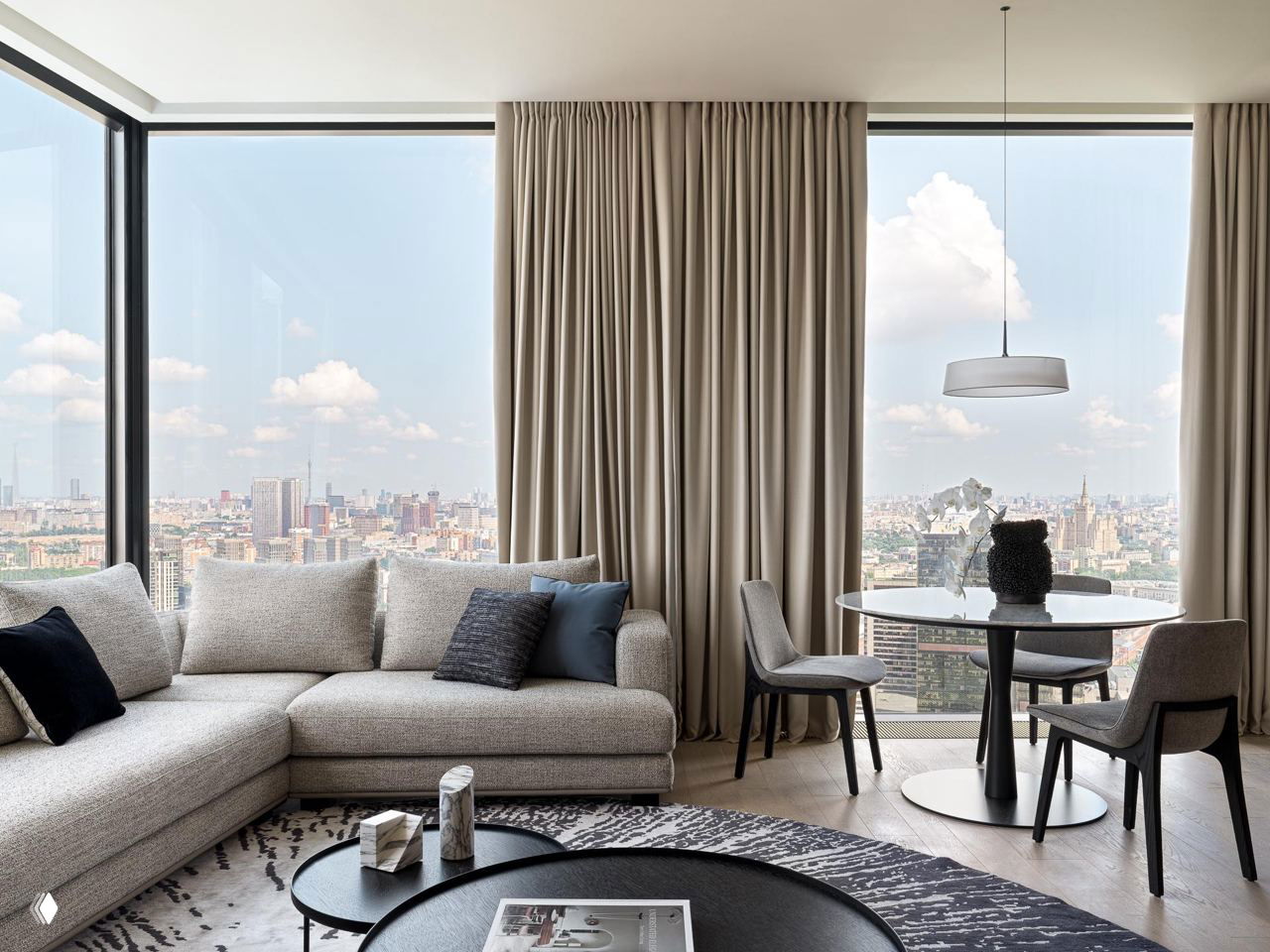 Гостиная с угловым диваном, нейтральным текстилем и синими декоративными подушками на фоне панорамного окна.