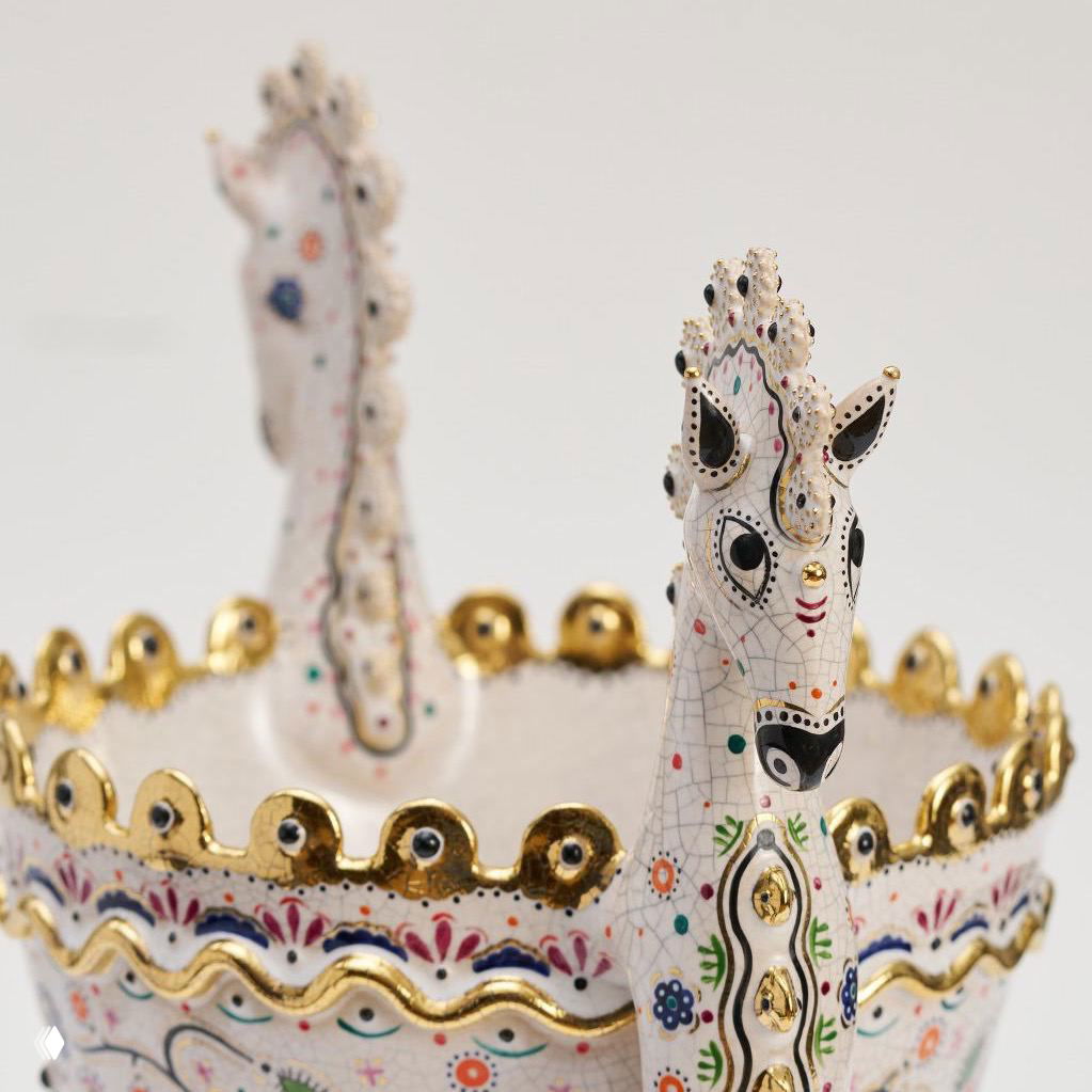 Крупный план белого керамического предмета с фигурой коня и золотой окантовкой, видны тонкие ручные росписи и текстура глазури.