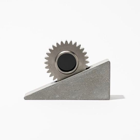 Альтернативный ракурс фоторамки с зубчатой шестернёй на бетонном основании, показывающий профиль и текстуру бетона на нейтральном фоне.