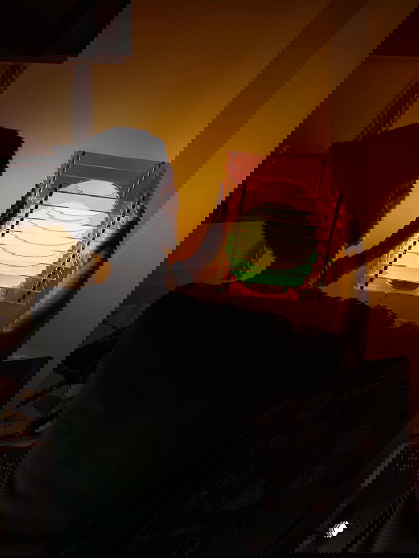 Человек держит лампу Dreamy Lop у стены: видно соотношение размеров, теплое разноцветное рассеянное свечение и систему акриловых панелей со стальными креплениями.