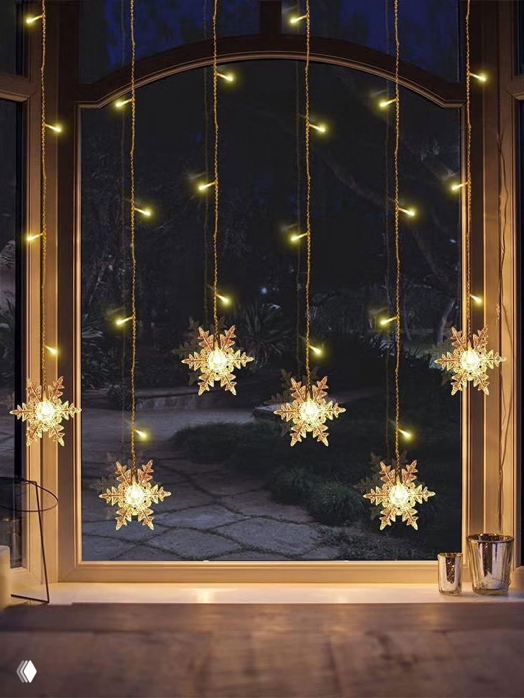 Подвесные светящиеся снежинки на длинных нитях перед тёмным окном — эффектная идея для вечерней подсветки и визуального оформления фасада или комнаты.
