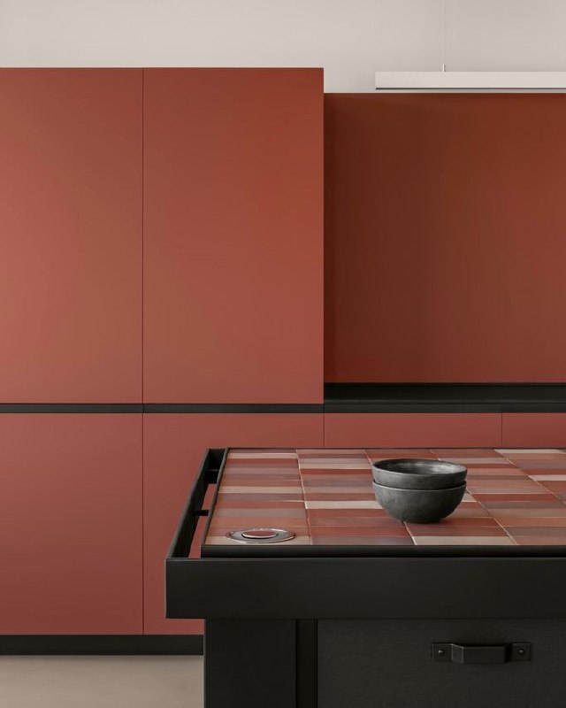 Фрагмент кухни с матовыми терракотовыми фасадами и рабочей поверхностью в чёрных тонах; акцент на плиточной столешнице в тёплой гамме и минимализме.