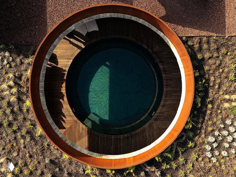 Аэрофотосъёмка круглого внутренних двора и бассейна Mimosa House: окружённая деревянной террасой цилиндрическая форма бассейна на фоне посадок.