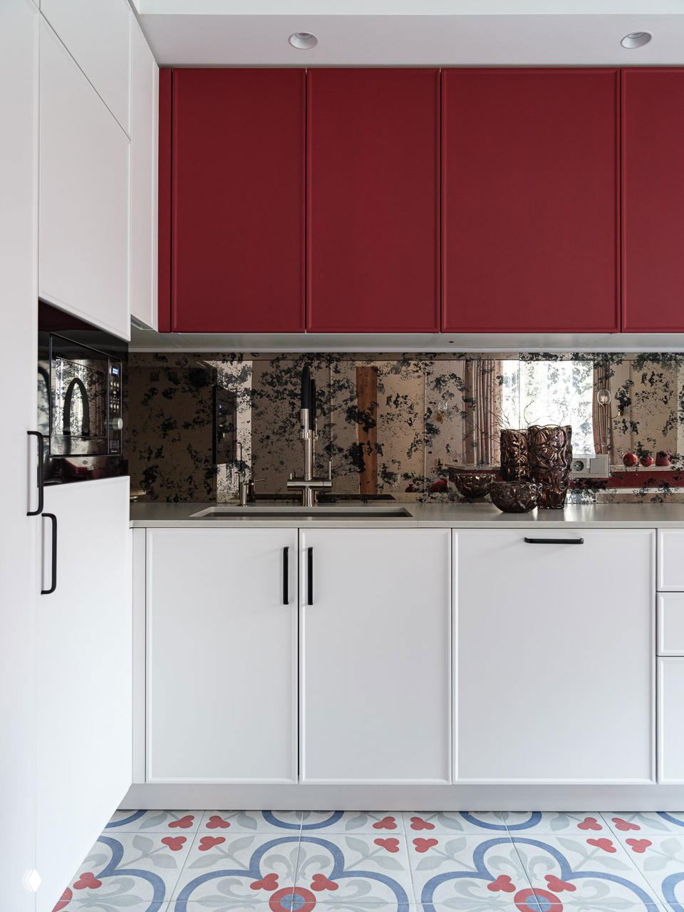 Кухонный фартук с зеркальным декоративным покрытием, белые нижние фасады и бордовые верхние шкафы на фоне узорной плитки пола.