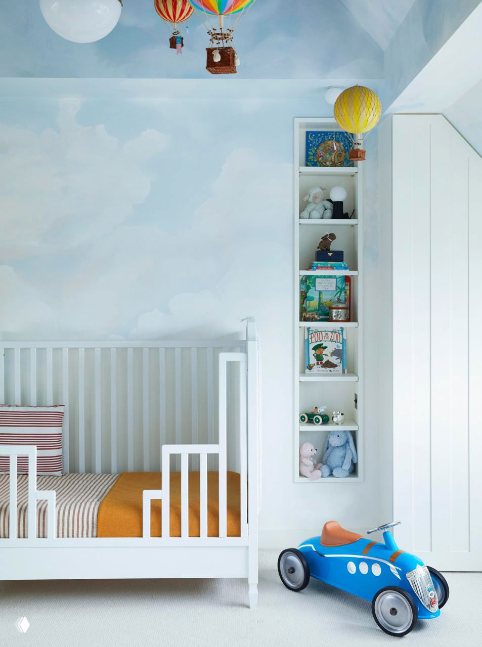 Светлая детская с белой кроваткой, потолком с росписью в облаках и декоративными подвесными моделями воздушных шаров над изголовьем для сказочной атмосферы.