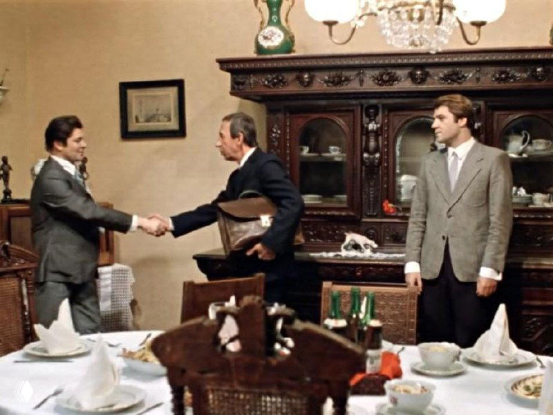 Кадр с антикварной мебелью и сервировкой на столе, композиция изображения частично искажена цифровыми артефактами, виден массивный сервант.