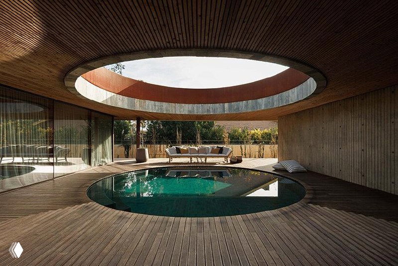 Круглый бассейн в центре двора дома, окружённый деревянной настилкой и нависающей крышей с круглым отверстием-люком для света и воздуха.