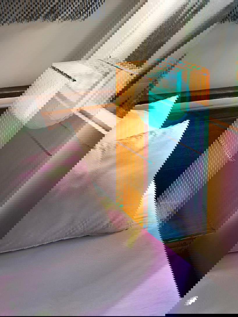 Лампа Dreamy Lop на прикроватной зоне: прозрачные акриловые пластины формируют цветные проекции и мягкий свет, контрастирующий с геометрией конструкции.