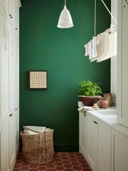 Узкая хозяйственная зона с зелёной стеной: компактная подвесная сушилка с несколькими предметами белья, плетёная корзина и рабочая поверхность.