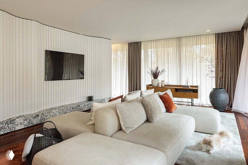 Светлая гостиная Mimosa House с мягким бежевым диваном, низким столом и большим остеклением, через которое виден внутренний двор и бассейн.