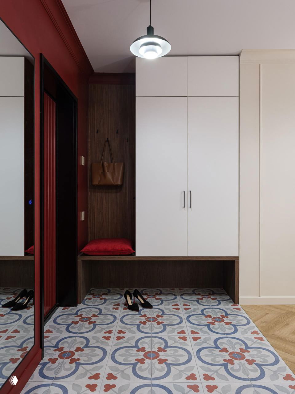 Прихожая с глубокими бордовыми акцентами, встроенными шкафами белого цвета и декоративной узорной плиткой на полу у входа.