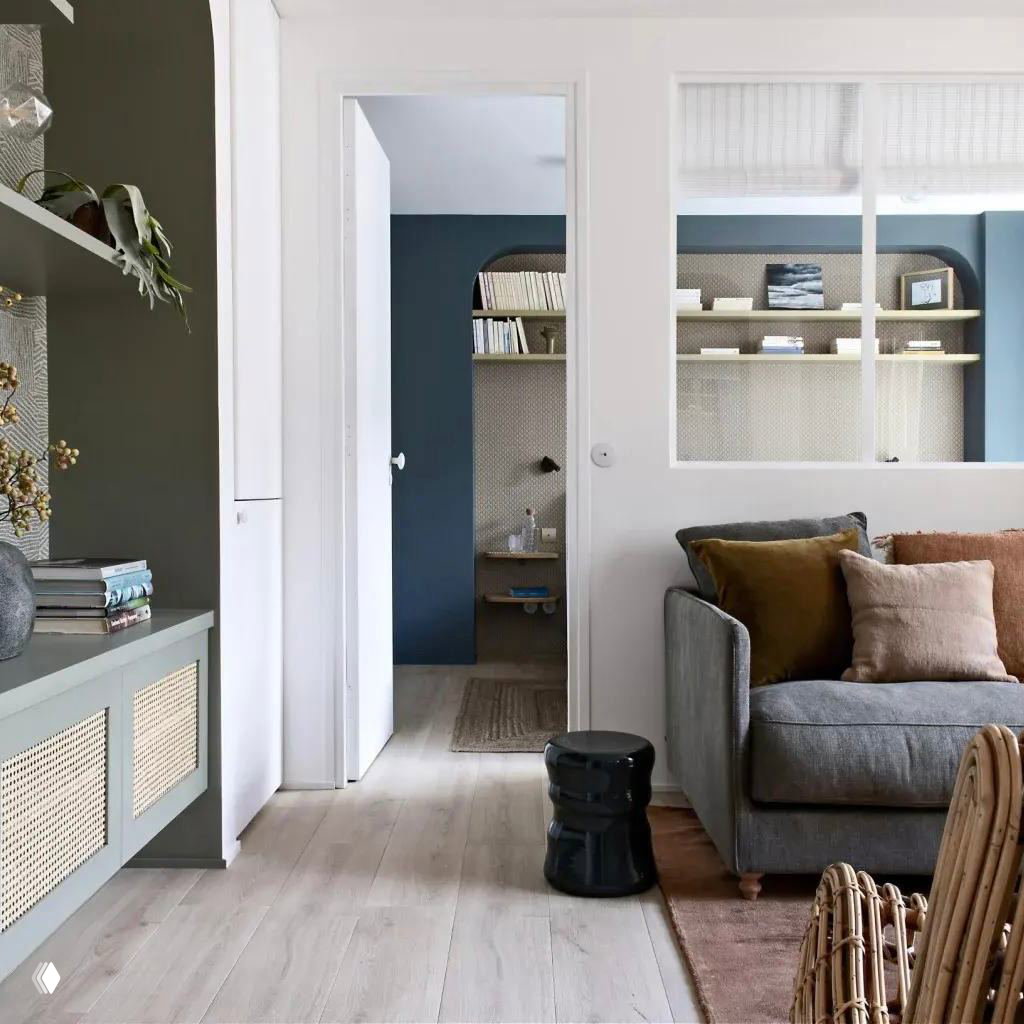 Проём с внутренним остеклением между комнатами, диван с бархатными подушками и вид на нишу с полками за арочной перегородкой.