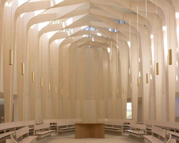 Интерьер часовни с высокими белыми арками, скамьями по периметру и мягким рассеянным светом, спокойная светлая атмосфера.