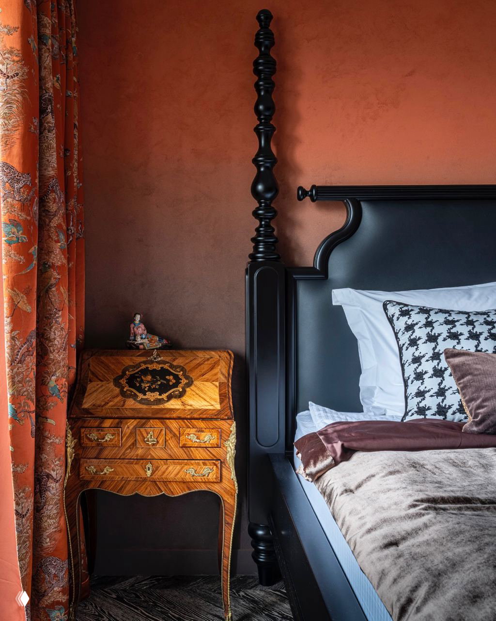 Спальня с богатой терракотовой отделкой и чёрной деревянной кроватью в классическом стиле; сочетание текстур, бархата и дерева создаёт уютный эффект.