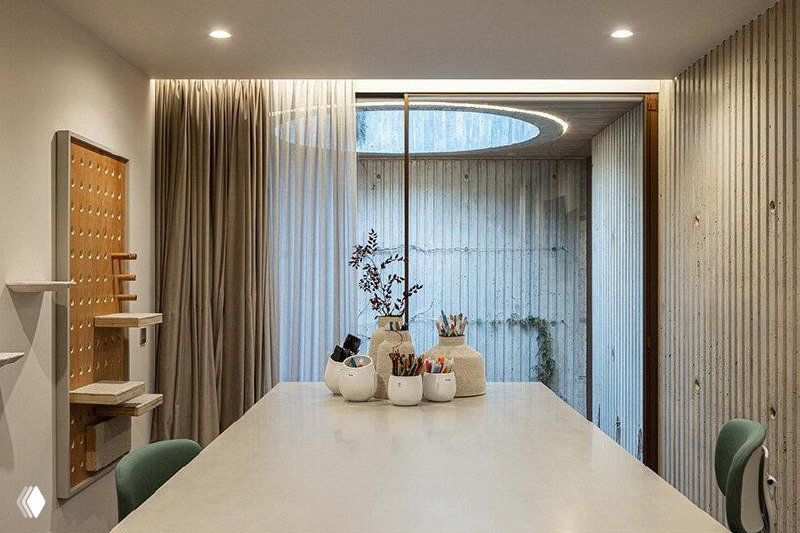 Небольшой рабочий кабинет с долгим столом, канцелярией на нём и стеклянной стеной, выходящей в маленький внутренний дворик с круговым световым окном.