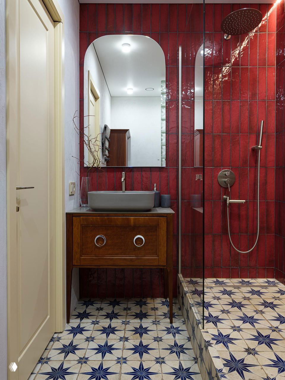 Ванная комната с яркой бордовой плиткой на стенах, душевой зоной и ретро-комодом под раковину на фоне мозаичного пола со звёздным орнаментом.