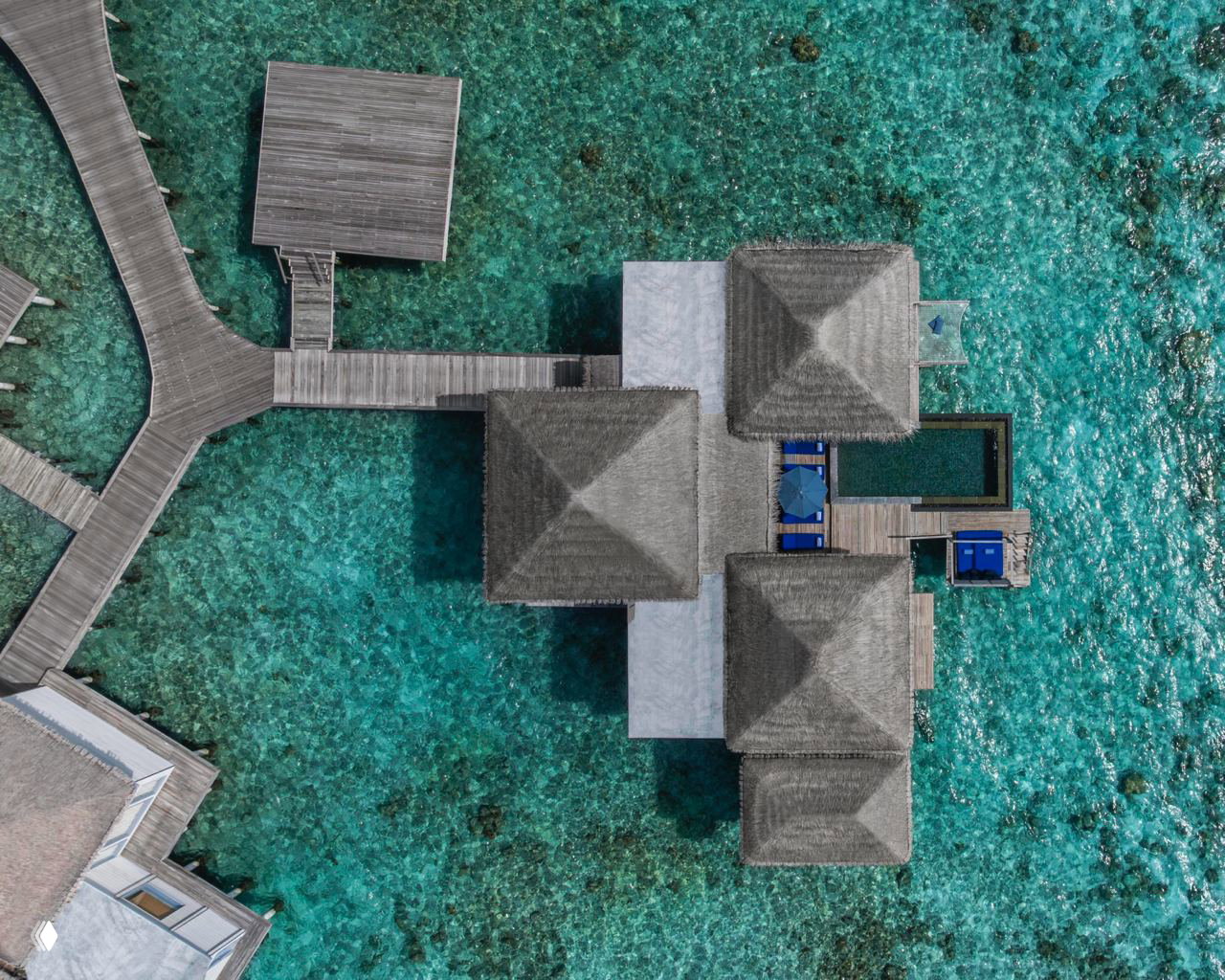 Аэрофото комплекса водных вилл The Halcyon Private Isles: деревянные настилы, причалы и кристально прозрачная морская вода вокруг вилл.
