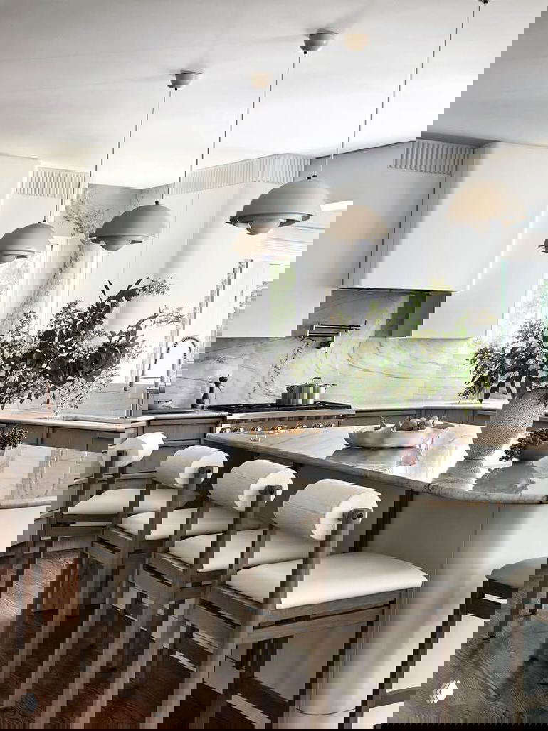 Светлая кухня с большим островом и мраморной столешницей, подвесными светильниками и рядом барных стульев в нейтральной палитре, с акцентом на материалы и форму.