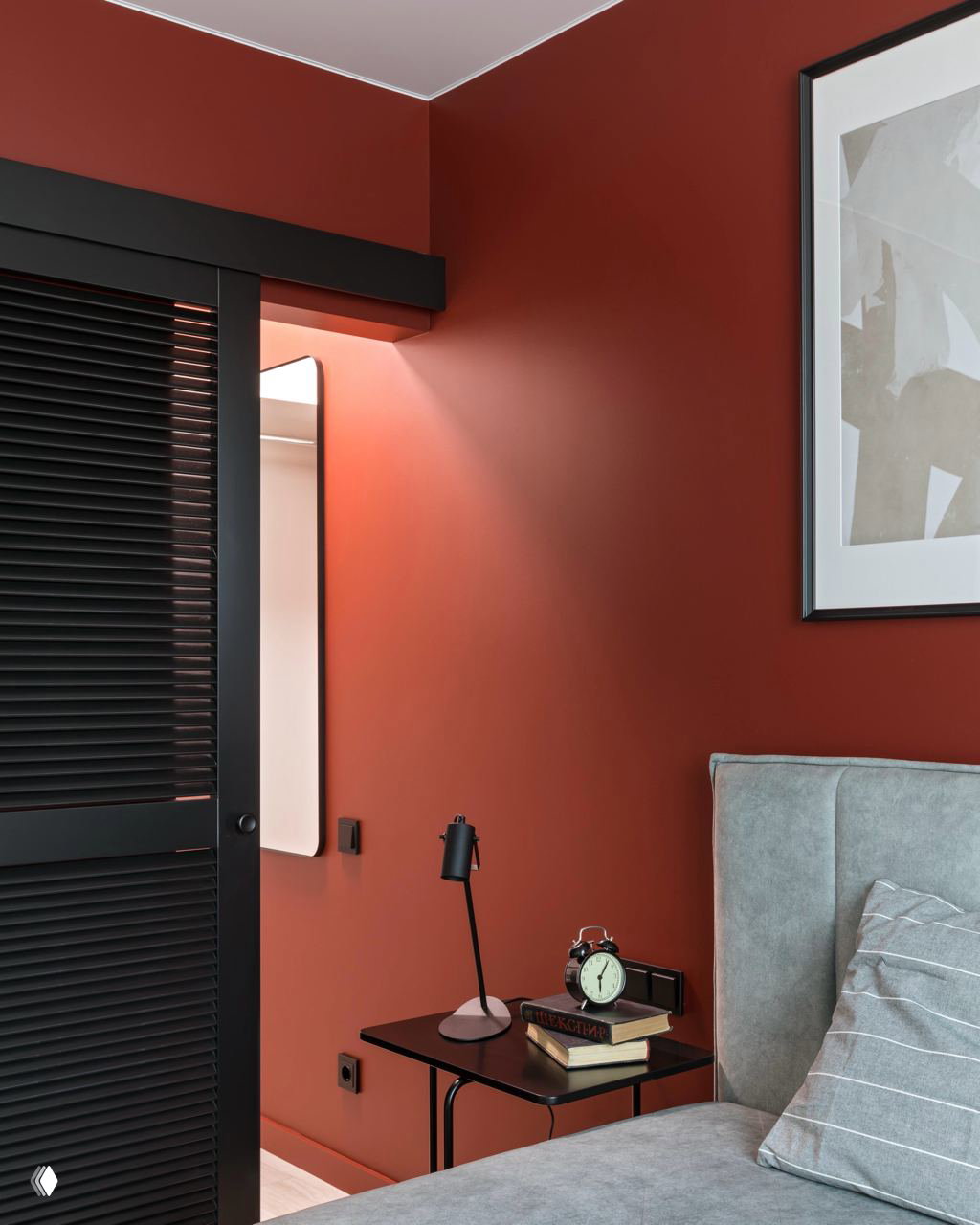 Спальная зона с матовыми терракотовыми стенами, чёрными шкафами и декоративными деталями в тёмной палитре — пример драматичного, но тёплого интерьера.