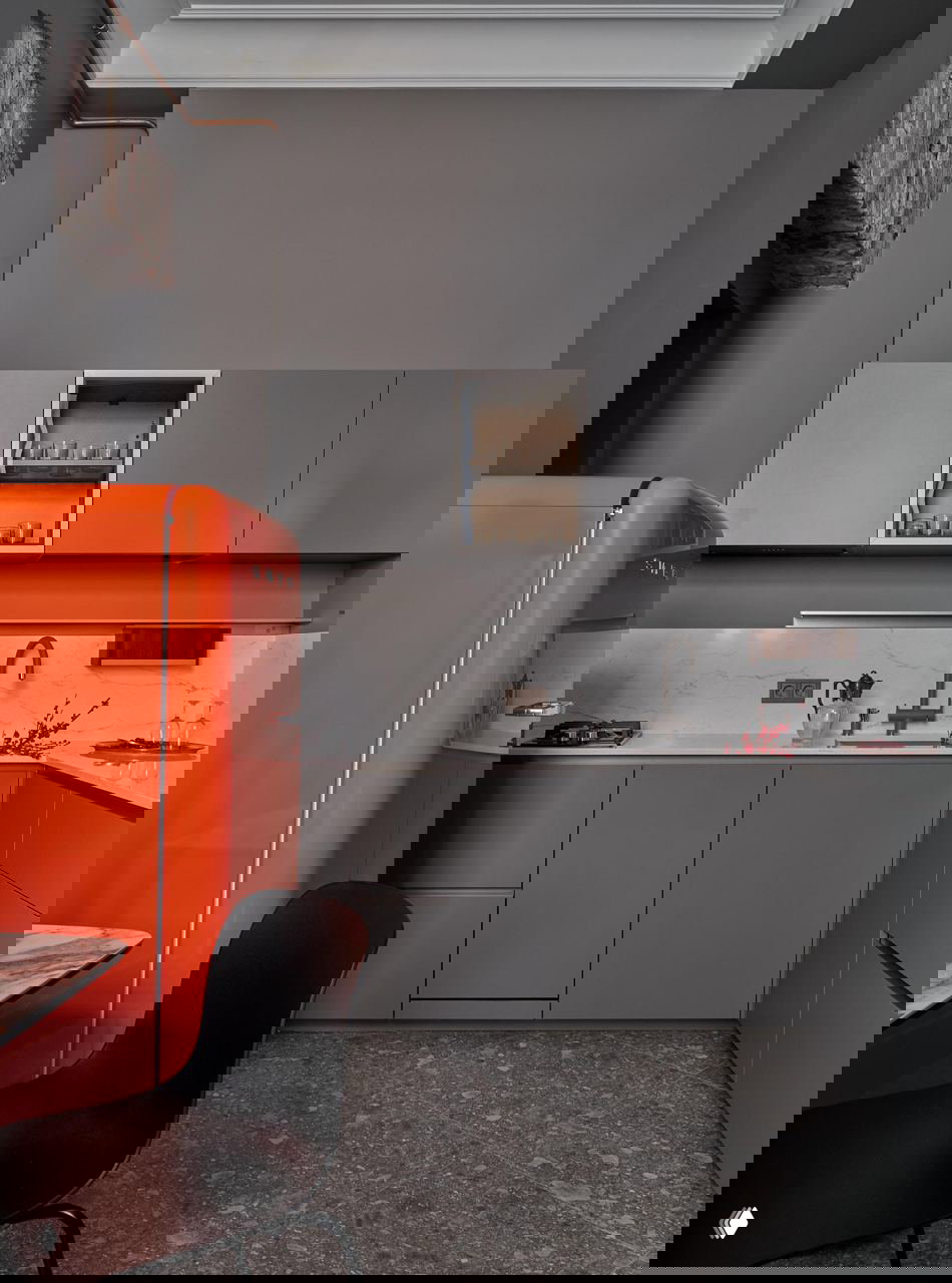 Кухня в серых тонах с ярко-оранжевым ретро-холодильником на переднем плане, сдержанные фасады и контрастная техника подчёркивают стильный акцент