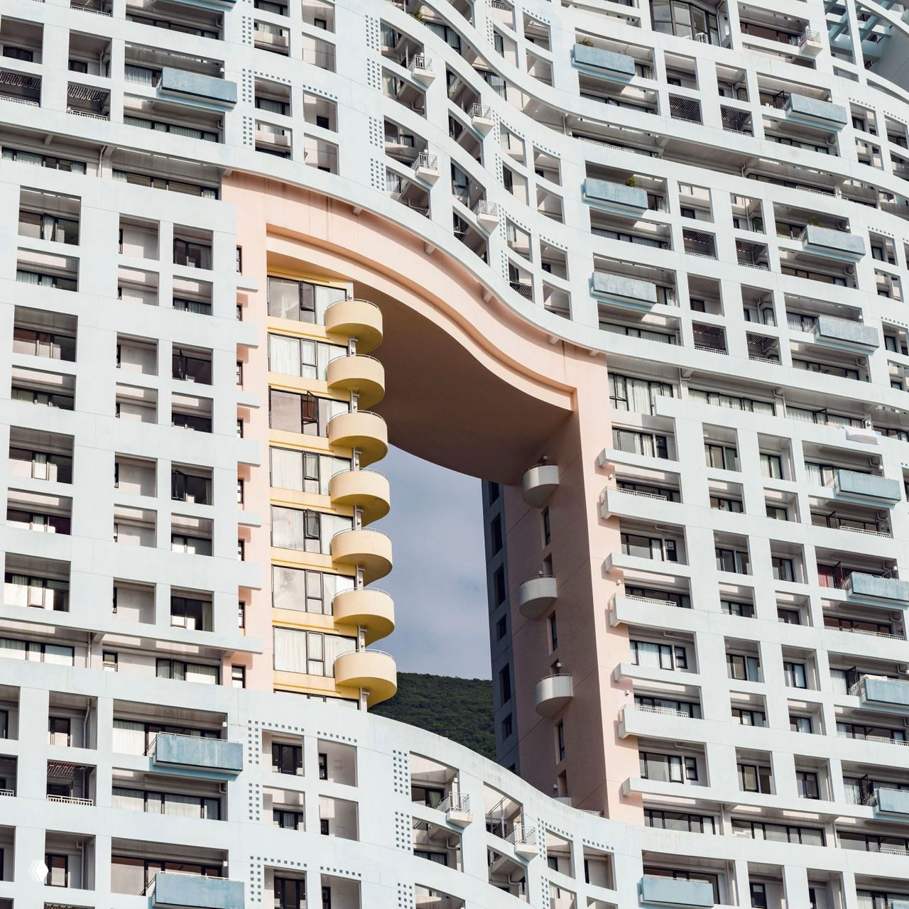 Фрагмент жилого комплекса в Гонконге с большим сквозным арочным отверстием в корпусе, видны балконы и регулярная сетка окон фасада.