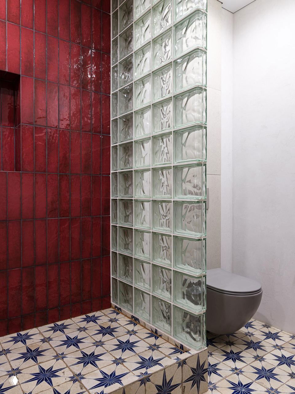 Душевая зона с перегородкой из стеклоблоков и туалетом: сочетание прозрачной кладки и узорной плитки пола в небольшой ванной.