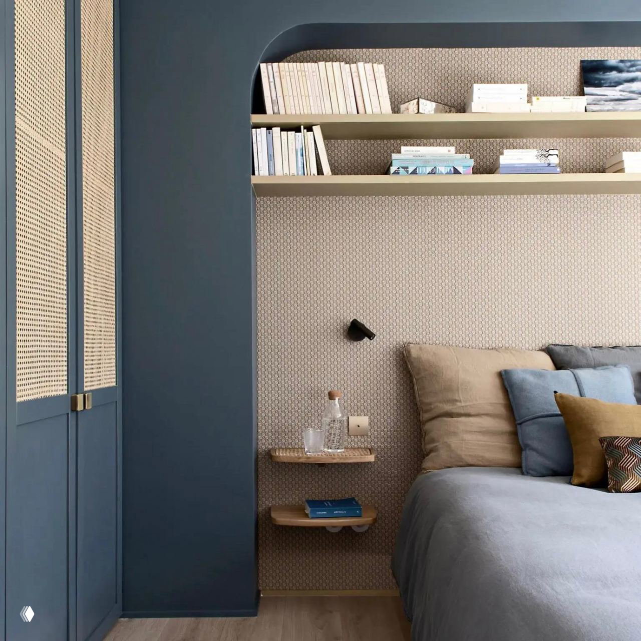 Спальная зона с арочным альковом и открытыми полками, синие шкафы с ротангом и аккуратная декоративная отделка вокруг кровати.