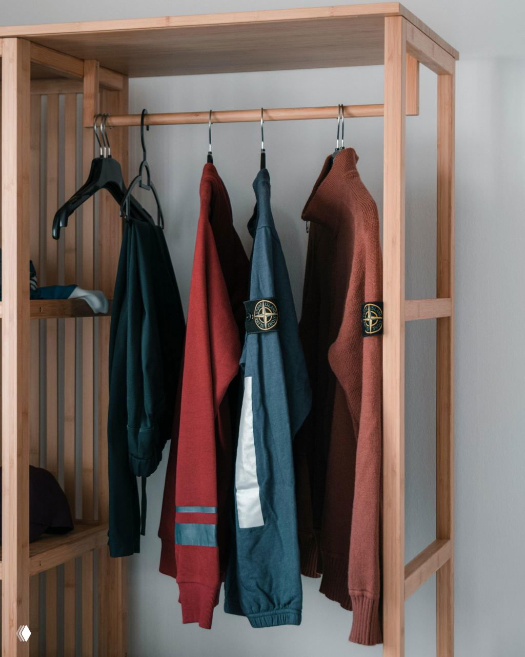 Открытая деревянная вешалка с одинаковыми вешалками и несколькими куртками — простой интерьерный приём для порядка и визуальной организации одежды.