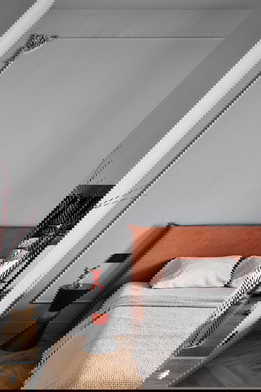 Спальная зона с серыми стенами и изголовьем в тёплом оранжево-коричневом тоне, небольшой прикроватный столик и минималистичный декор в спокойной палитре