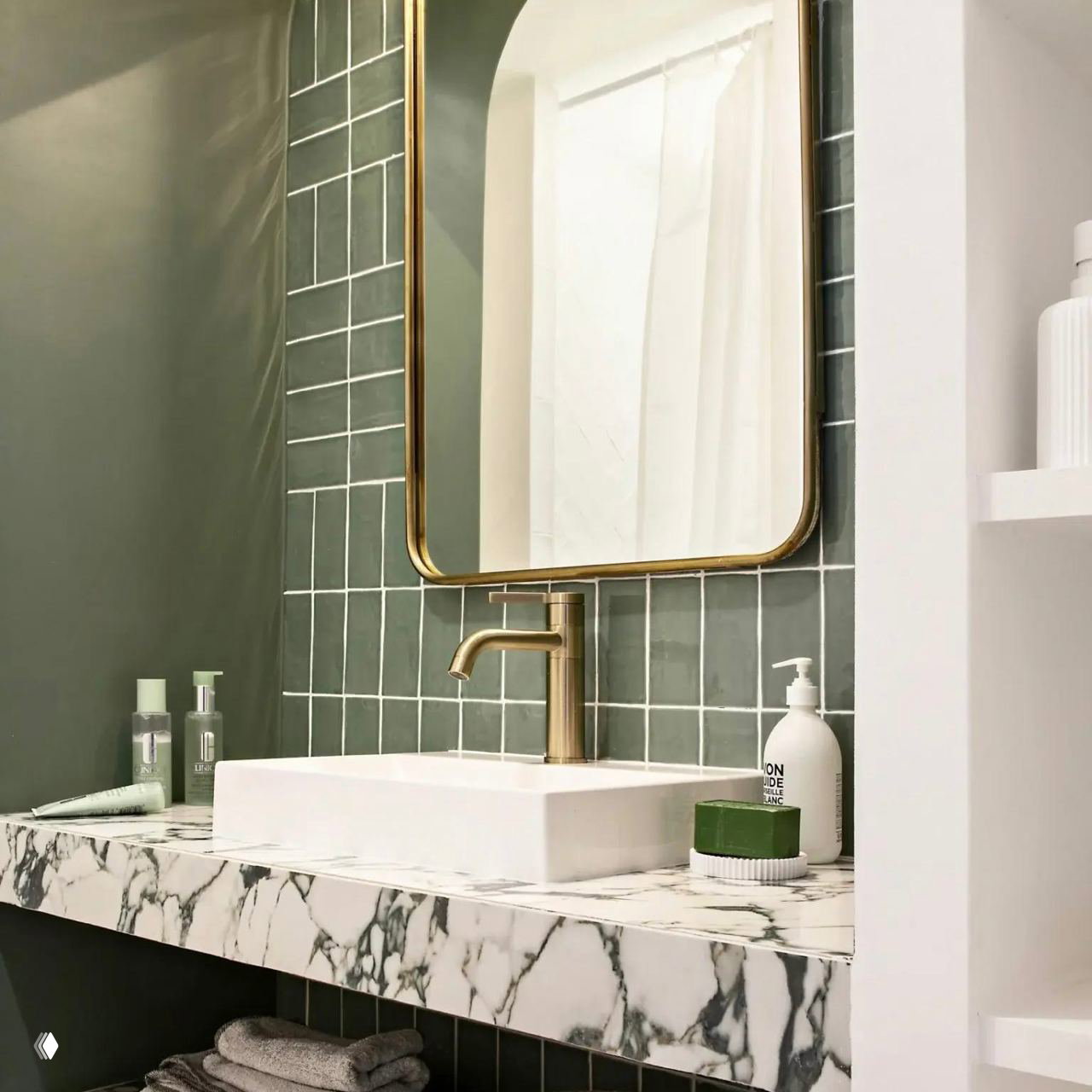 Ванная с зелёной плиткой, мраморной столешницей и золотым смесителем; кадр показывает зеркало и раковину в элегантной отделке.