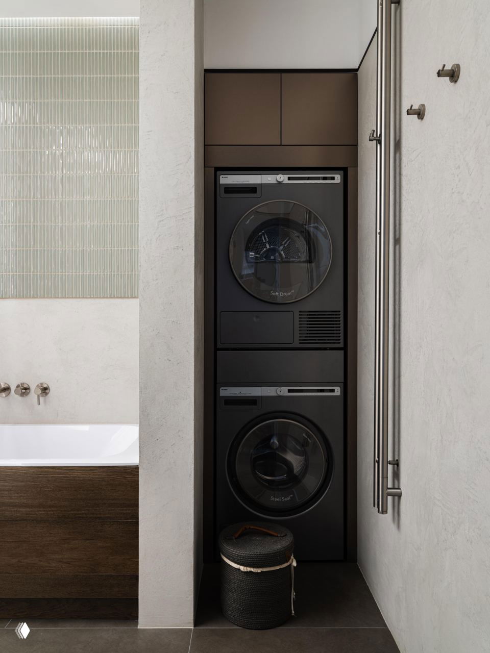 Ниша с вертикально установленной стиральной машиной и сушкой в компактном санузле; чёрная техника и минималистичная стилистика экономят пространство квартиры.